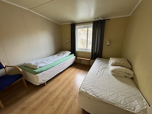 Gemütliches Schlafzimmer in Hitra, Norwegen, mit zwei Einzelbetten, Holzfußboden und Naturblick durch ein großes Fenster. Ideal für entspannte Angelurlaube in der spektakulären norwegischen Natur.