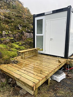 Kleine Holzhütte mit Veranda in Nordland, Norwegen, umgeben von moosbewachsenen Felsen und herbstlicher Landschaft. Ideal für Angelurlaube und Naturerlebnisse in ruhiger, abgeschiedener Umgebung.