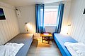 Gemütliches Zimmer in Nordland, Norwegen, mit Holzwänden, zwei Einzelbetten, blauem Vorhang und Fenster. Ideal für Angler auf Angelreise, die nach einer komfortablen Unterkunft suchen. Entspannen nach spannenden Angeltagen.