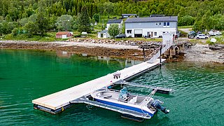 Ein modernes Boot dockt an einem Steg in der ruhigen Bucht an. Umgeben von üppigem Grün und einem gemütlichen Haus in Norwegen. Ideal für Angelabenteuer.