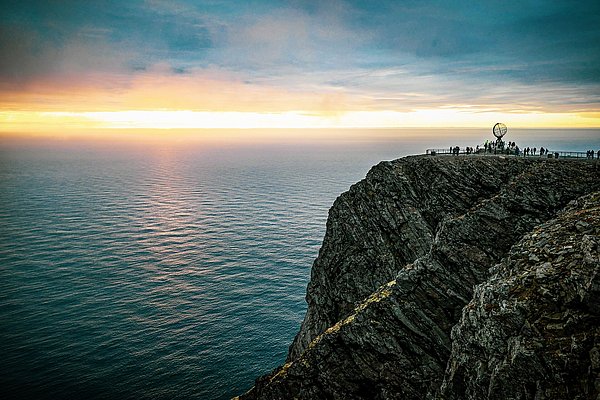 Beeindruckender Ausblick am Nordkap in Nord-Norwegen: Steile Klippen treffen auf die unendlichen Weiten des Ozeans, während ein leuchtender Sonnenuntergang den Himmel färbt. Perfektes Ziel für Abenteuer und Naturerlebnisse.