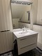 Ein modernes, helles Badezimmer in Nord-Norwegen mit elegantem Waschbecken, Spiegel mit Beleuchtung und weiß getäfelten Wänden. Perfekte Mischung aus skandinavischem Design und Funktionalität für entspannende Aufenthalte in einer malerischen Umgebung.