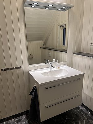 Ein modernes, helles Badezimmer in Nord-Norwegen mit elegantem Waschbecken, Spiegel mit Beleuchtung und weiß getäfelten Wänden. Perfekte Mischung aus skandinavischem Design und Funktionalität für entspannende Aufenthalte in einer malerischen Umgebung.