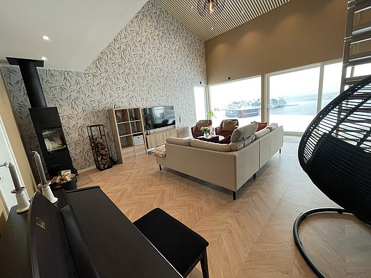 Wohnzimmer in Hitra, Norwegen: Gemütliches Sofa, Kamin, große Fenster mit Meerblick. Modernes skandinavisches Design, das Ruhe und Entspannung verspricht. Perfekt für Angelurlaub und Erholung in idyllischer Umgebung an der norwegischen Küste.