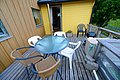 Gemütliche Terrasse eines Holzhauses in Nord-Norwegen, mit Glasstisch und Stühlen, umgeben von grüner Natur. Ideal für entspannte Abende nach aufregenden Angeltouren in dieser idyllischen Umgebung. Perfekte Kulisse für einen Angelurlaub.