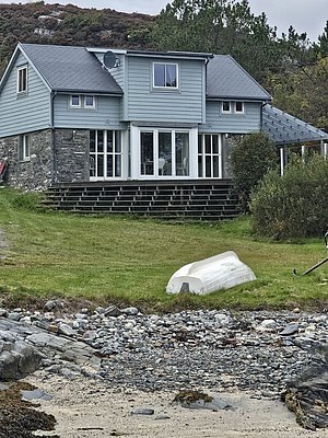 Gemütliches Haus in Südwest-Norwegen, idyllisch am Küstenufer gelegen. Ideal für Angelreisen. Vor dem Haus liegt ein umgedrehtes Boot, eingebettet in grüner Landschaft und felsiger Küste. Perfekter Ausgangspunkt für Abenteuer.