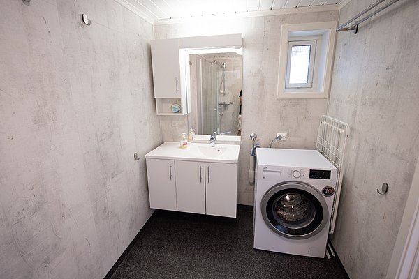 Ein modernes Badezimmer mit Waschmaschine, weißem Waschtisch und Spiegel in einem hellen Raum mit grauen Wänden.