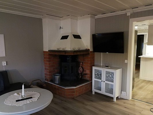 Gemütliches Wohnzimmer mit Kamin, Wand-TV, weißem Schrank und rundem Tisch mit Kerze.