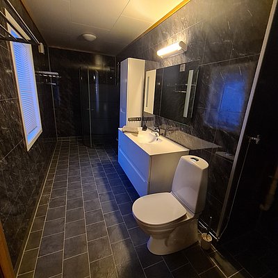 Modernes Badezimmer in Nord-Norwegen mit schwarzer Fliesenoptik, weißem Waschbecken und WC. Stilvolle Beleuchtung sorgt für harmonische Atmosphäre. Perfekt für einen komfortablen Angelurlaub in skandinavischem Design.