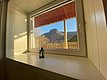 Blick aus einem gemütlichen Raum in Nord-Norwegen: Durch ein Fenster sieht man eine malerische Berglandschaft im Sonnenlicht, eine Laterne schmückt die Fensterbank. Perfekt für einen erholsamen Angelurlaub.