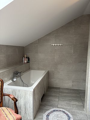 Modernes skandinavisches Badezimmer in Nord-Norwegen mit grauen Fliesen, Badewanne, Holzverkleidung und dekorativem Teppich. Perfekt für Erholung nach einem erfolgreichen Angeltag in der nördlichen Wildnis.