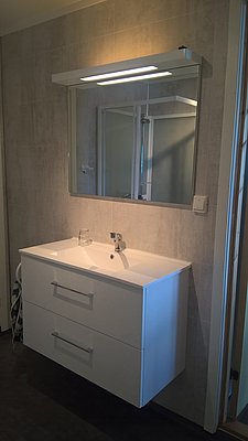 Modernes Badezimmer in Nord-Norwegen mit elegantem weißen Waschtisch, Spiegel und integrierter Beleuchtung. Ideal für Komfort und Entspannung nach einem erfolgreichen Angeltrip in der malerischen norwegischen Wildnis.