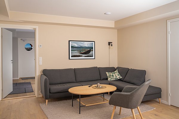 Gemütliches Wohnzimmer auf Hitra, Norwegen: moderne graue Couch, Holztisch, stilvolles Bild von Boot an der Wand. Perfekte Unterkunft für Angelurlauber, die Entspannung und Abenteuer suchen. Skandinavisches Design für wohlige Atmosphäre.