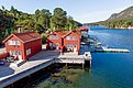 Rote Holzhäuser am Wasser auf Hitra, Norwegen, idyllische Lage mit Bootssteg; perfekte Basis für Angelurlaub. Malerische Landschaft, klare Fjorde und erholsame Natur laden zum Entspannen ein. Perfekter Startpunkt für Meeresangeln und Outdoor-Abenteuer.