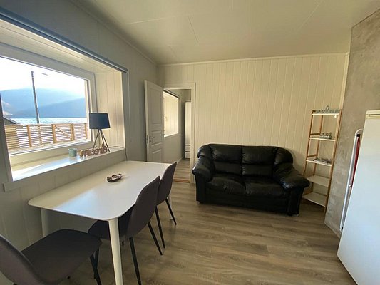 Gemütliche Ferienwohnung in Nord-Norwegen mit stilvollem Interieur, Ledersofa und Esstisch. Großes Fenster mit Blick auf fjordähnliche Landschaft. Ideal für Angelurlaube und Erholung in unberührter Natur. Perfekter Rückzugsort für Abenteurer und Entspannungssuchende.