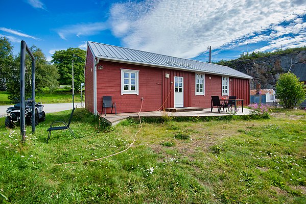 Rotes Holzhaus in Nord-Norwegen: Umgeben von grüner Landschaft und strahlendem Himmel bietet es eine idyllische Atmosphäre für Angelreisen. Perfekt für den Urlaub in der Natur und Nähe zu fischreichen Gewässern.