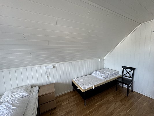Gemütliches Schlafzimmer auf Hitra, Norwegen: Zwei Einzelbetten, Holzboden, weiße Holzverkleidung, minimalistisch eingerichtet. Ideal für Erholung nach einem erlebnisreichen Angeltag. Perfekt für Angelreisende, die Komfort und Einfachheit schätzen.
