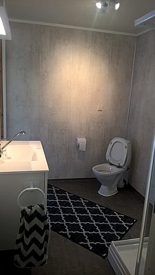 Modernes Badezimmer in Nord-Norwegen mit stilvollem Waschbecken, WC und Dusche. Neutrale Farben und geometrischer Teppich schaffen eine einladende Atmosphäre. Ideal für Angelreisende, die Komfort und Entspannung suchen.