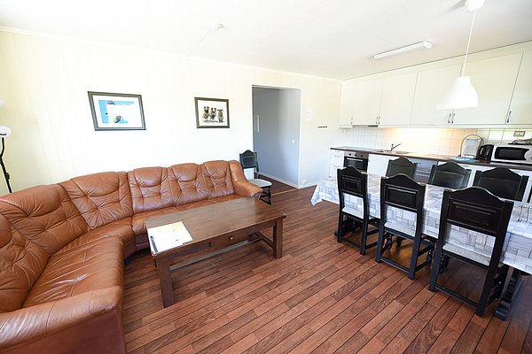 Gemütliches Apartment auf Hitra, Norwegen. Offene Küche, Esszimmer mit Holzmöbeln und braunem Ledersofa. Ideale Unterkunft für Angelurlauber, die Komfort und Funktionalität schätzen. Perfekt für entspannte Abende nach einem erfolgreichen Angeltag.