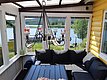 Eine gemütliche Veranda mit schwarzem Sofa und Tisch bietet einen Panoramablick auf einen ruhigen See mit angrenzendem grünen Wald.