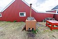 Rote Holzhütte in Hitra, Norwegen, mit Outdoor-Ofen und Holzstapel. Perfektes Angelurlaubsziel für Natur- und Entspannungsfreunde. Ideal für Ausflüge und gemütliche Abende im Freien.