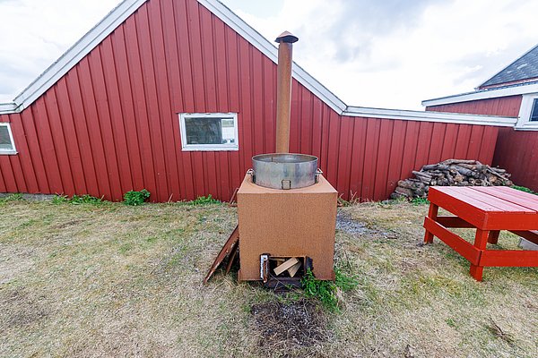 Rote Holzhütte in Hitra, Norwegen, mit Outdoor-Ofen und Holzstapel. Perfektes Angelurlaubsziel für Natur- und Entspannungsfreunde. Ideal für Ausflüge und gemütliche Abende im Freien.