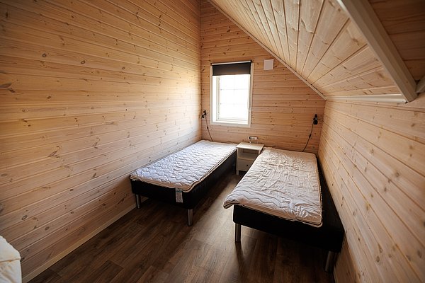 Gemütliches Schlafzimmer in Nordland, Norwegen: Helle Holzwände, zwei Einzelbetten, kleiner Nachttisch, Dachschräge, Fenster mit Tageslicht. Perfekt für entspannende Angelreisen und Erholung in idyllischer Naturkulisse.