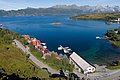 Küstenlandschaft in Nordland, Norwegen: Rote Holzhäuser und ein Pier am blauen Fjord vor majestätischen Bergen. Perfekter Ort für einen Angelurlaub, umgeben von atemberaubender Natur. Ideal für Erholung und Abenteuer.