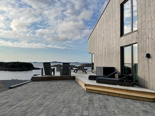Moderne Holzterrasse am Wasser mit gemütlichen Sitzgelegenheiten, Aussicht auf die idyllische Küstenlandschaft von Hitra, Norwegen. Der perfekte Ort für einen entspannten Angelurlaub in atemberaubender Naturkulisse.