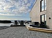 Moderne Holzterrasse am Wasser mit gemütlichen Sitzgelegenheiten, Aussicht auf die idyllische Küstenlandschaft von Hitra, Norwegen. Der perfekte Ort für einen entspannten Angelurlaub in atemberaubender Naturkulisse.