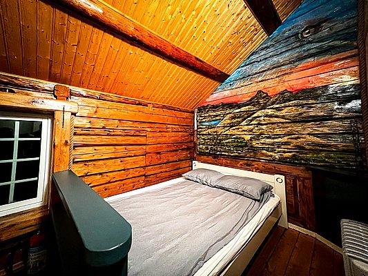 Gemütliches Holzinterieur in norwegischem Ferienhaus auf Hitra. Rustikales Schlafzimmer mit Bett und kunstvoll bemalter Wand. Ideal für Angelurlaub und Erholung in der Natur.
