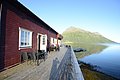 Rotes Holzhaus in Nordland, Norwegen, am klaren Fjord. Weite Terrasse, umgeben von ruhiger Natur und Bergen. Perfekt für Angelurlaub und Outdoor-Abenteuer in traumhafter skandinavischer Kulisse.