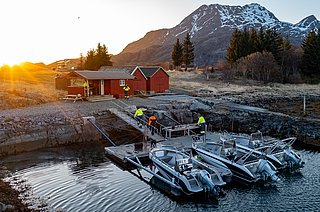Kleiner Hafen in Südwest-Norwegen: Rote Holzhäuser am Ufer, Boote im klaren Wasser, umgeben von Bergen im Abendlicht. Perfekter Ort für einen erholsamen Angelurlaub mit atemberaubender Natur und idealen Fangbedingungen.