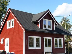 Rotes Holzhaus in Nordland, Norwegen, bei sonnigem Wetter. Traditionelle Architektur mit schwarzen Schindeldach und weißen Fensterrahmen. Ideal für Angelfans, die skandinavische Idylle suchen. Perfekter Standort für unvergessliche Angelreisen und Naturerlebnisse.