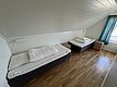 Gemütliches Zimmer in Hitra, Norwegen: Zwei Einzelbetten mit weißer Bettwäsche, helle Holzvertäfelung, blaugrüne Vorhänge und Holzboden. Einladend für Angelabenteuer in idyllischer Umgebung. Ideal für erholsame Nächte nach aufregenden Angeltouren.