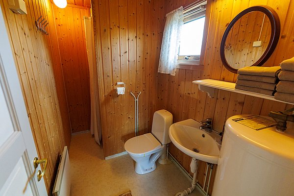 Holzvertäfeltes Badezimmer in Hitra, Norwegen. Ausstattung: kleine Dusche, Toilette, Waschbecken, Spiegel, Handtücher. Gemütlich und funktional für Angelurlauber. Natürliche Materialien schaffen rustikales Ambiente in skandinavischem Stil. Perfekt für Abenteuer mit Komfort.