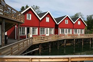 Rote Holzhäuser am Wasser in Nordland, Norwegen – perfekte Unterkunft für Angler. Gemütlich und direkt an der Küste gelegen. Entdecke die beeindruckende Natur und erlebe unvergessliche Angelabenteuer in malerischer Umgebung.