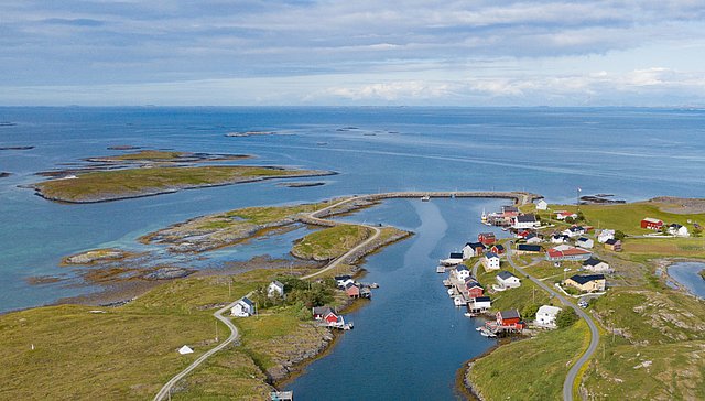 Luftaufnahme der malerischen Küstenlandschaft in Nordland, Norwegen. Kleine, bunte Häuser und klare Wasserwege zwischen grünen Inseln unter blauem Himmel verbreiten Idylle und einladende Angelmöglichkeiten. Perfekt für Angelreisen und Natururlaub.