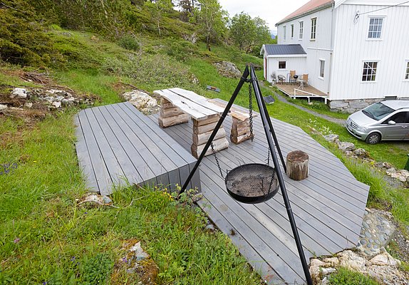 Holzterrasse in Hitra, Norwegen mit rustikalen Sitzmöbeln und einem Grillplatz, umgeben von grüner Natur. Perfekt für einen gemütlichen Angelurlaub und entspannende Stunden im Freien. Ideal gelegen, um die Schönheit Norwegens zu genießen.