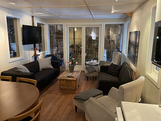 Gemütlicher Wohnbereich in Hitra, Norwegen: Moderne Einrichtung mit komfortablen Sofas, Holztisch, Fernseher und großen Fenstern. Ideal für Entspannung nach einem Angelabenteuer. Perfekt für Angelreisen und Entdecker der norwegischen Küstenregion.