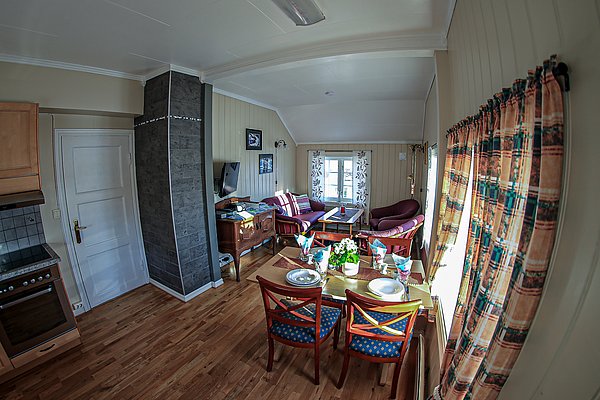 Gemütliches Wohnzimmer in Nord-Norwegen, Holzmöbel, Esstisch, gemütliche Couch, helle Fenster, rustikale Holzoptik, ideal für Angelurlaube. Perfekt für Entspannung nach erlebnisreichen Angelausflügen.