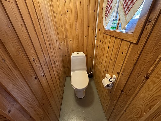 Kompaktes Badezimmer mit Holzwänden in Hitra, Norwegen. Gemütliches Ambiente mit Kiefernholzverkleidung, schlichtem Fenster und moderner Toilette. Erlebe norwegische Tradition und Komfort auf deiner Angelreise.