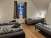 Gemütliches Schlafzimmer in Nord-Norwegen: Drei Einzelbetten mit floralem Bettzeug, Holzfußboden, weiße Wände. Fenster mit Vorhängen, weiches Licht. Ideale Unterkunft für Angelreisen oder Outdoor-Abenteuer. Entspannung in skandinavischer Atmosphäre.
