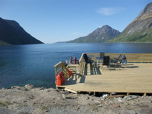 Holzterrasse mit Blick auf einen Fjord in Nordland, Norwegen. Umgeben von Bergen, lädt diese idyllische Kulisse zum Angeln und Entspannen ein. Perfekter Ort für Angelurlaube und Naturerlebnis. Ideal für Abenteuer und Erholung in skandinavischer Natur.