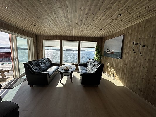Gemütliches Wohnzimmer mit Ledersofas und Panoramablick auf das Meer. Helle Holzverkleidung ergänzt die skandinavische Atmosphäre. Perfekter Rückzugsort in Hitra, Norwegen, ideal für entspannende Angelreisen.
