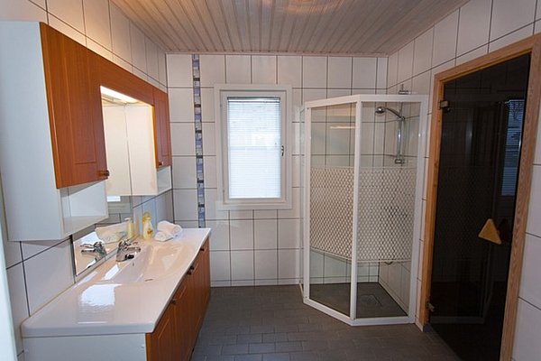 Modernes Badezimmer in Nord-Norwegen mit weißen Fliesen, großem Waschbecken, Duschkabine und Sauna. Helle Holzoberflächen sorgen für eine einladende Atmosphäre. Ideal nach einem erfolgreichen Angeltag in der atemberaubenden nordischen Landschaft.