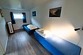Gemütliches Schlafzimmer in Nordland, Norwegen, mit zwei Einzelbetten und minimalistischem Design. Helle Wände, blau bezogene Betten, Fenster mit blauen Vorhängen und dekorativen Landschaftsbildern an den Wänden. Ideal für ruhigen Angelurlaub.