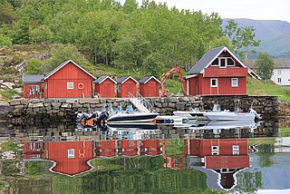 Rote Holzhäuser spiegeln sich im ruhigen Wasser von Hitra, Norwegen. Boote liegen am Ufer an. Ein idyllischer Standort für Angelreisen und Naturerlebnisse in skandinavischer Landschaft. Perfekt für Meeresangeln und Erholung in Norwegen.