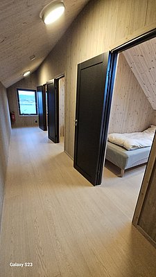 Heller Flur in norwegischem Ferienhaus auf Hitra. Holzverkleidete Wände, drei Türen, großes Fenster mit Meeresblick. Gemütliches Schlafzimmer sichtbar. Ideal für Angelurlaub und Erholung in Norwegen.