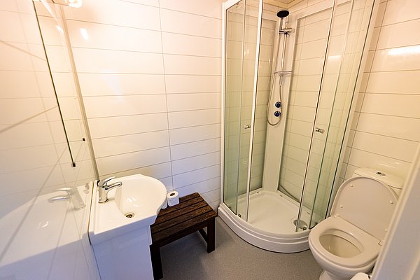 Modernes Badezimmer in Nordland, Norwegen: Helle Fliesen, Glasdusche, Waschbecken, Toilette und Holzbank. Ideal für einen komfortablen Angelurlaub. Sauber und praktisch gestaltet. Perfekter Ort zur Entspannung nach einem Tag voller Abenteuer.